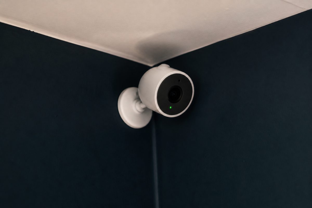 White indoor Wi-Fi security camera mounted high on a dark wall
