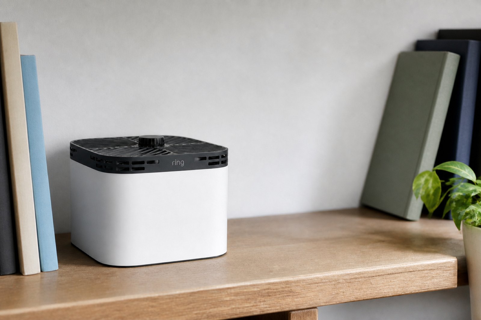 Ring Always Home Cam docked in its white cube base station on a shelf, the dark charcoal drone disc with a fully perforated rim nested into the dock so the camera lens is hidden.