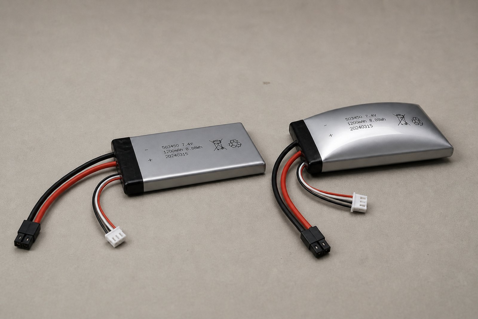 Two shrink wrapped lithium polymer battery packs side by side on a bench, the left one flat with square edges and the right one domed upward into a smooth taut bulge.