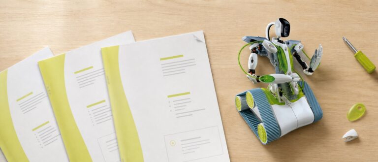 Overhead view of a workbench with three stapled A4 manuals in white and lime green fanned out beside a white and green tracked robot with a camera head on a gooseneck.