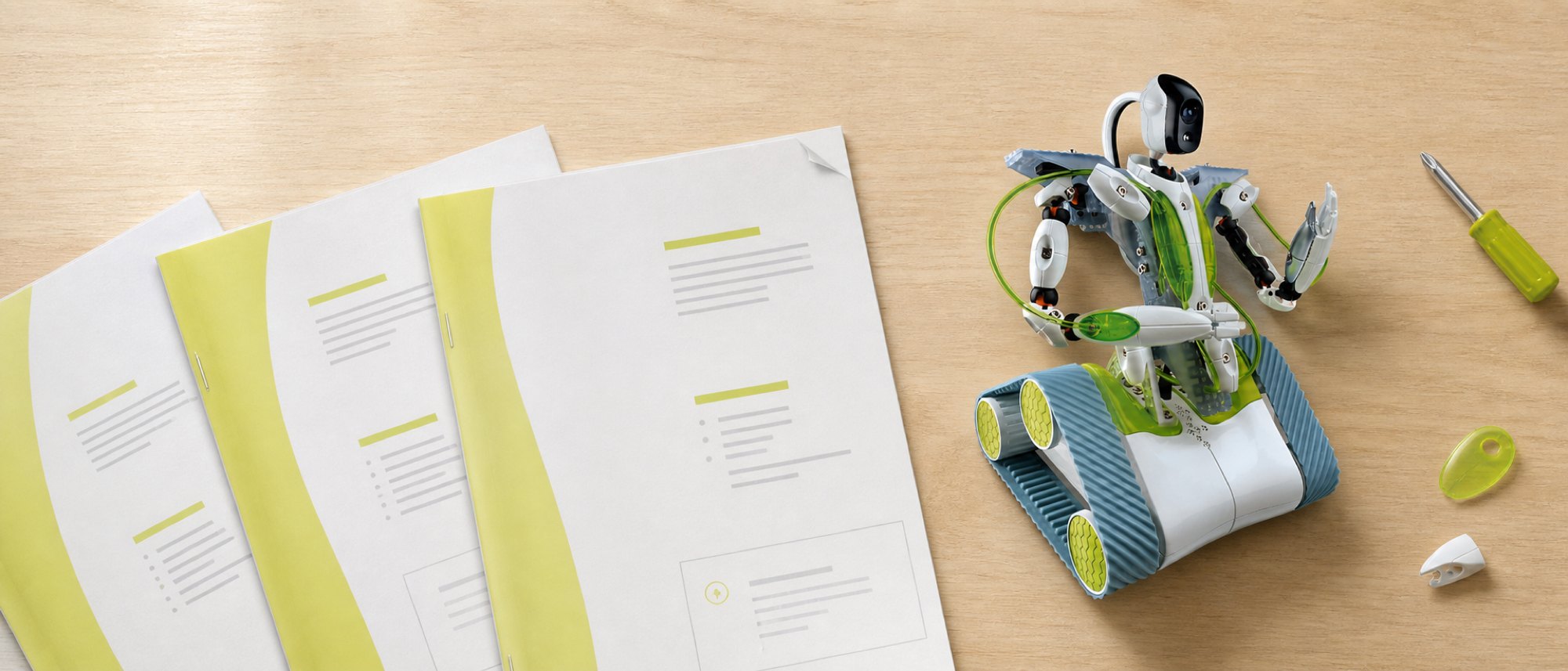Overhead view of a workbench with three stapled A4 manuals in white and lime green fanned out beside a white and green tracked robot with a camera head on a gooseneck.