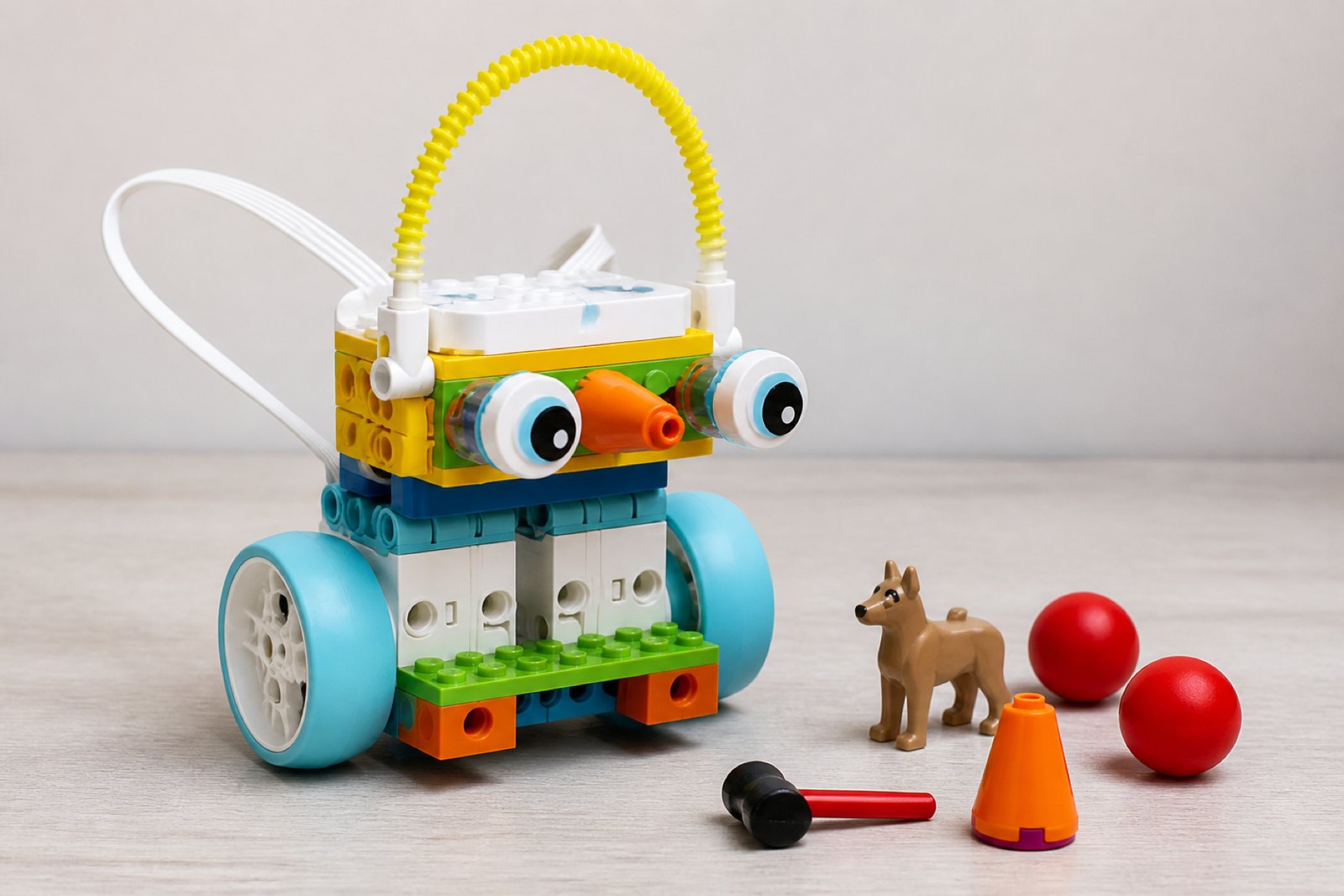 A brick built creature on four chunky teal wheels with two large white domed eyes on stalks, an orange cone nose and a coiled yellow spring arcing over its head, with a red ball, an orange cone and a small brick dog beside it.